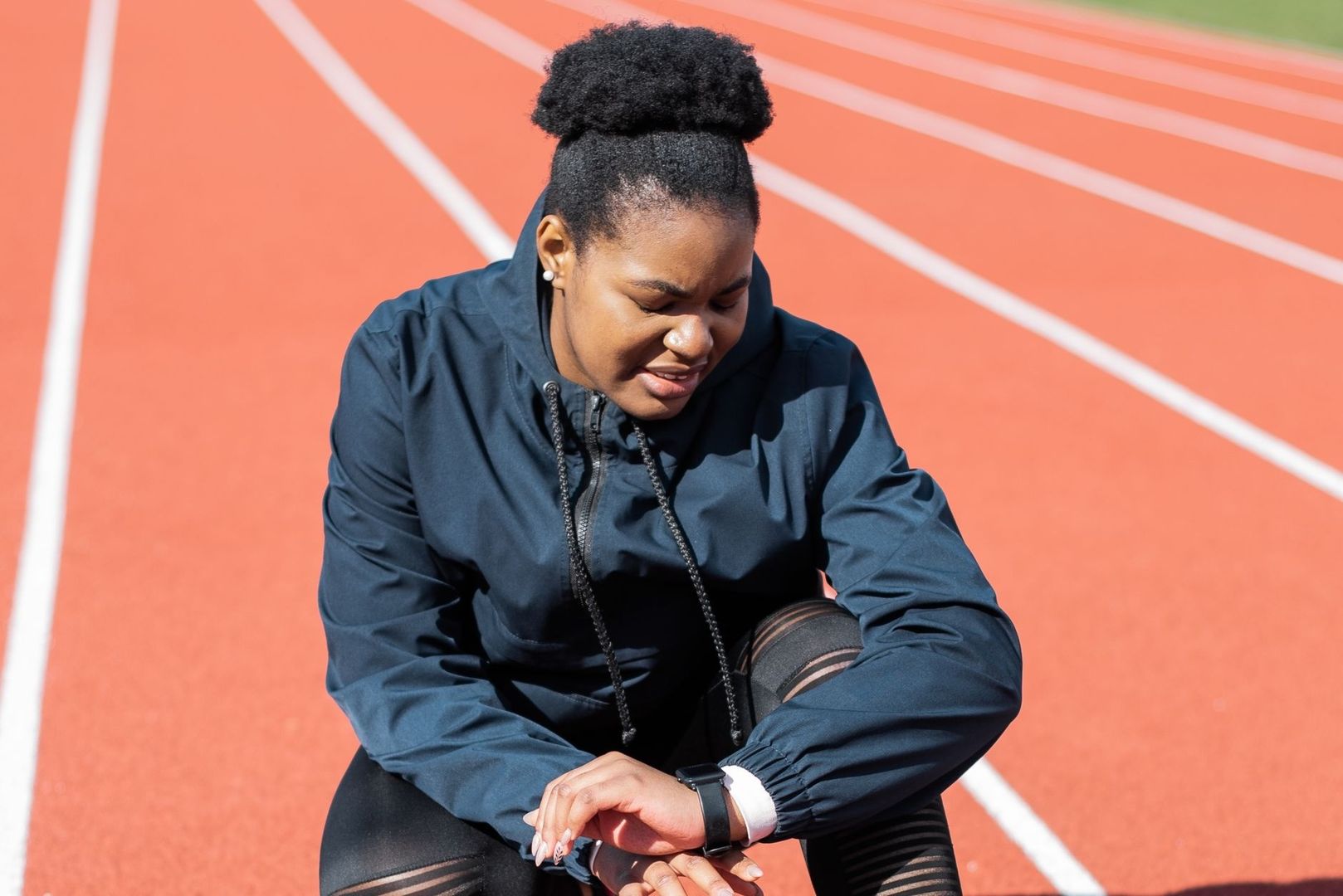 Sportive assise sur une piste, consultant sa montre connectée